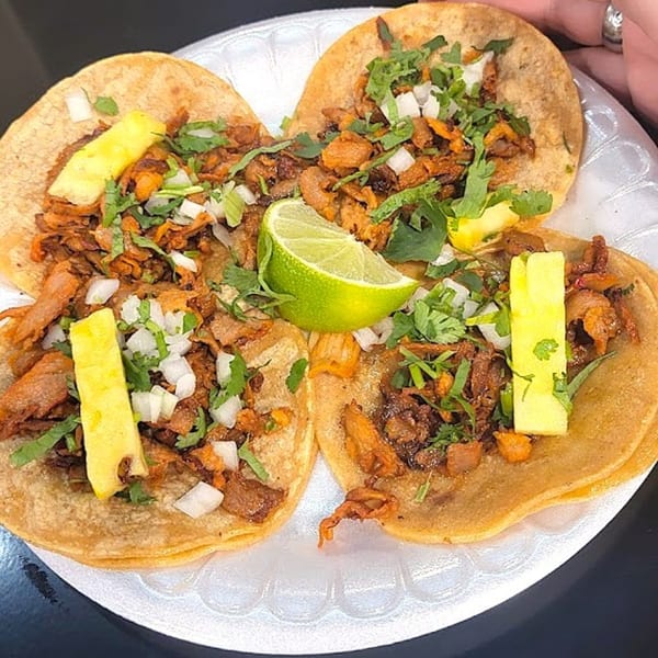 Three Holy Taco al pastor tacos with pineapple, cilantro, onion, and lime on a white plate.