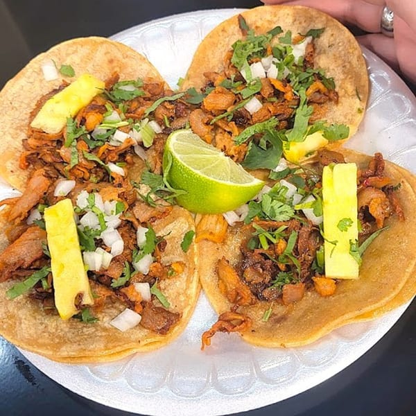Three Holy Taco al pastor tacos with pineapple, cilantro, and onions on a white plate.