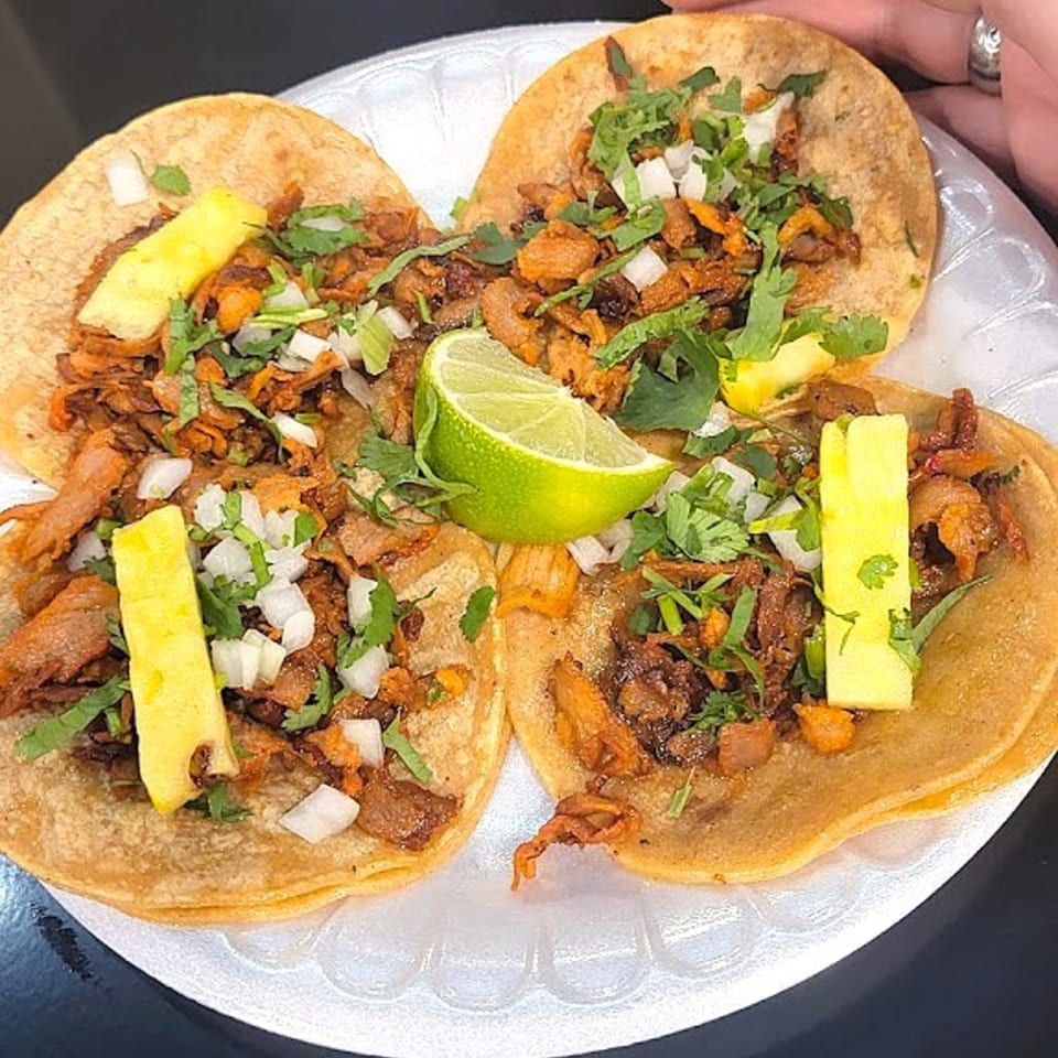 Three Holy Taco al pastor tacos with pineapple, cilantro, and onions on a white plate.