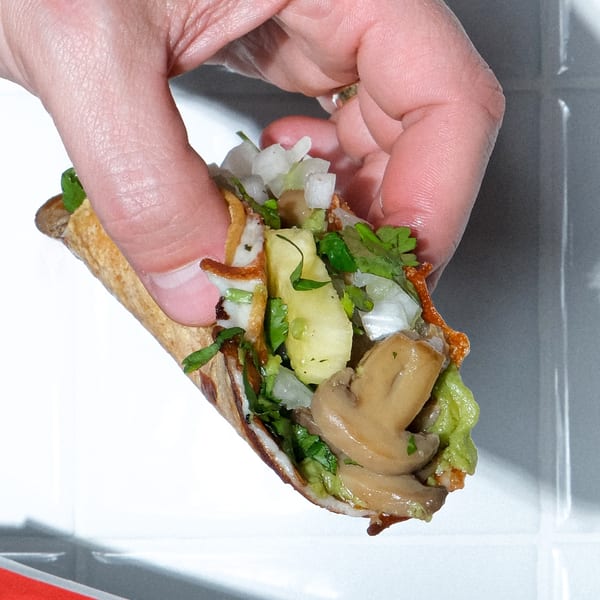 A hand holds a Holy Taco with mushrooms, pineapple, onions, and cilantro.