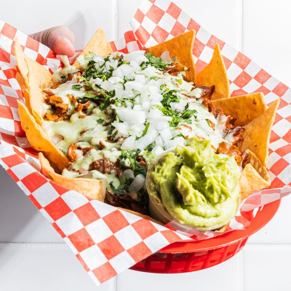 Holy Taco's nachos with meat, green sauce, onions, cilantro, and a side of guacamole.