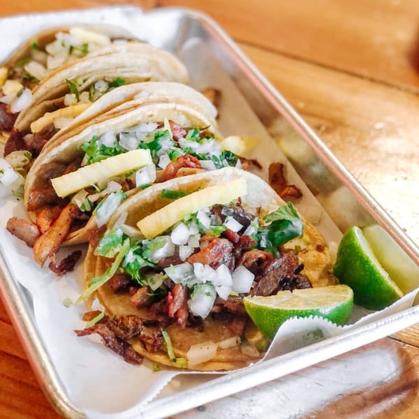 Holy Taco's tray of al pastor tacos with pineapple, onions, cilantro, and lime wedges.