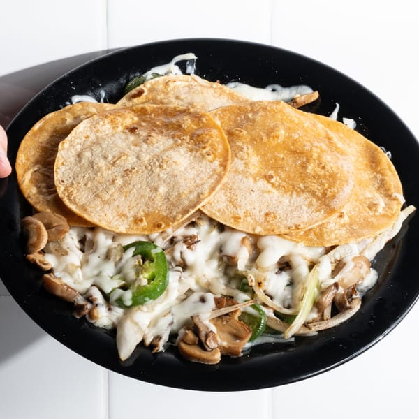 Holy Taco's cheesy mushroom and jalapeño tacos on a black plate with corn tortillas.